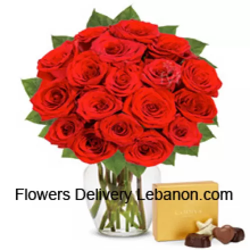 24 rosas rojas con algunos helechos en un florero de vidrio acompañadas de una caja de chocolates importados