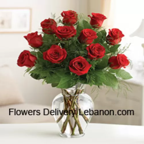 12 rosas rojas con algunos helechos en un jarrón de vidrio